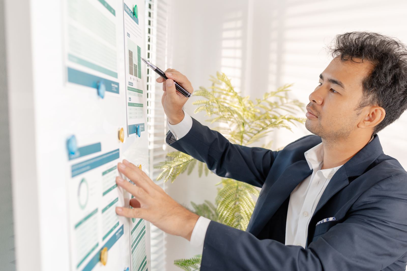 A man in a suit analysing charts pinned to a wall in a bright office