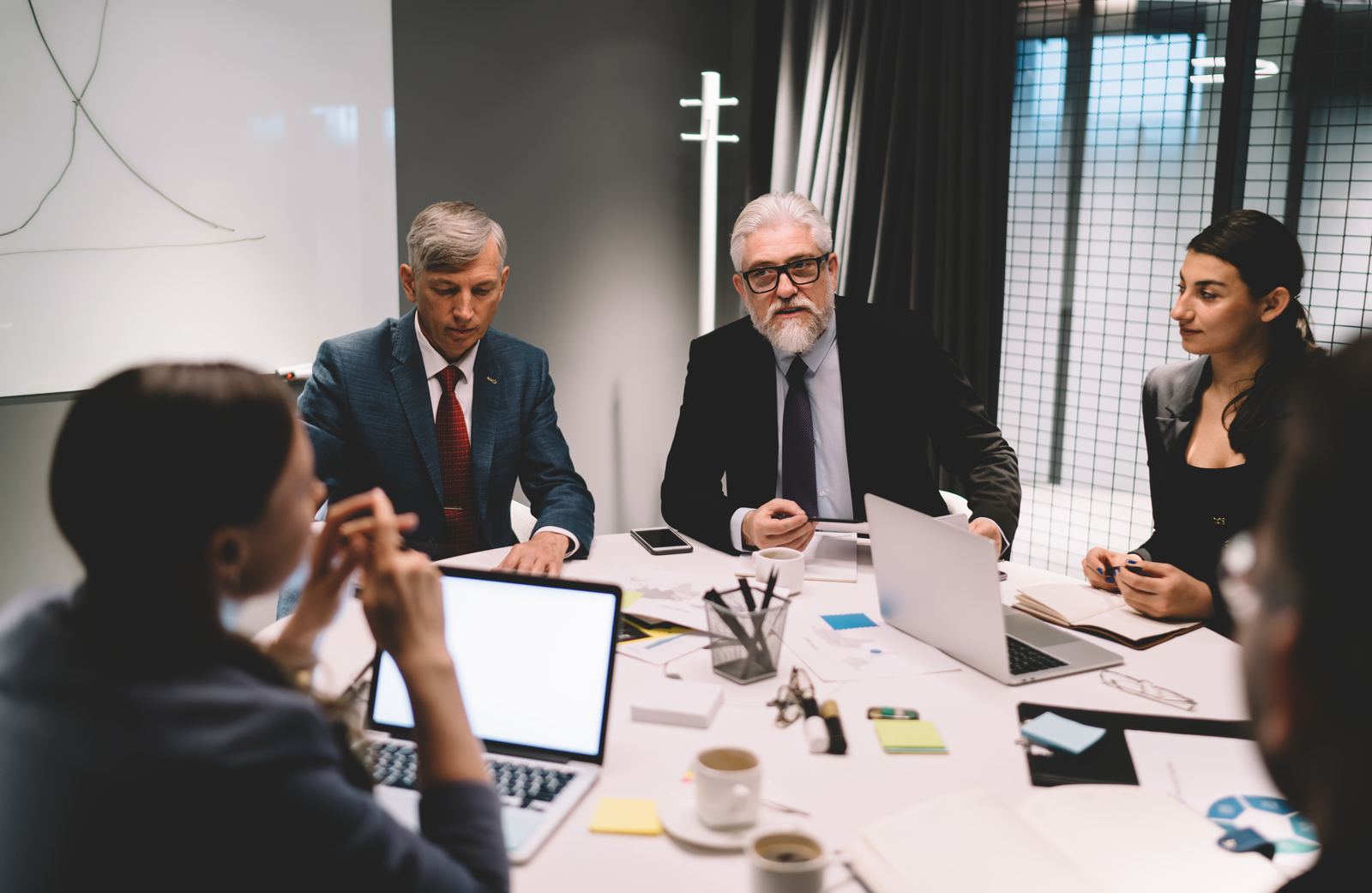 A team meeting at a conference table with laptops, two senior managers listening at the head of the table