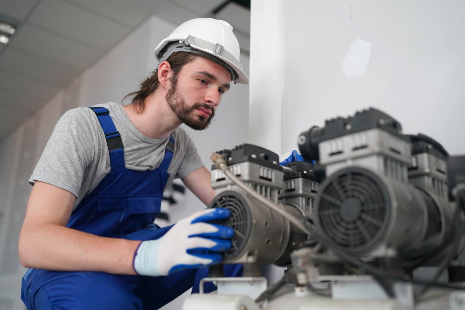 An engineer in a hard hat inspecting a compressor unit in an industrial plant room
