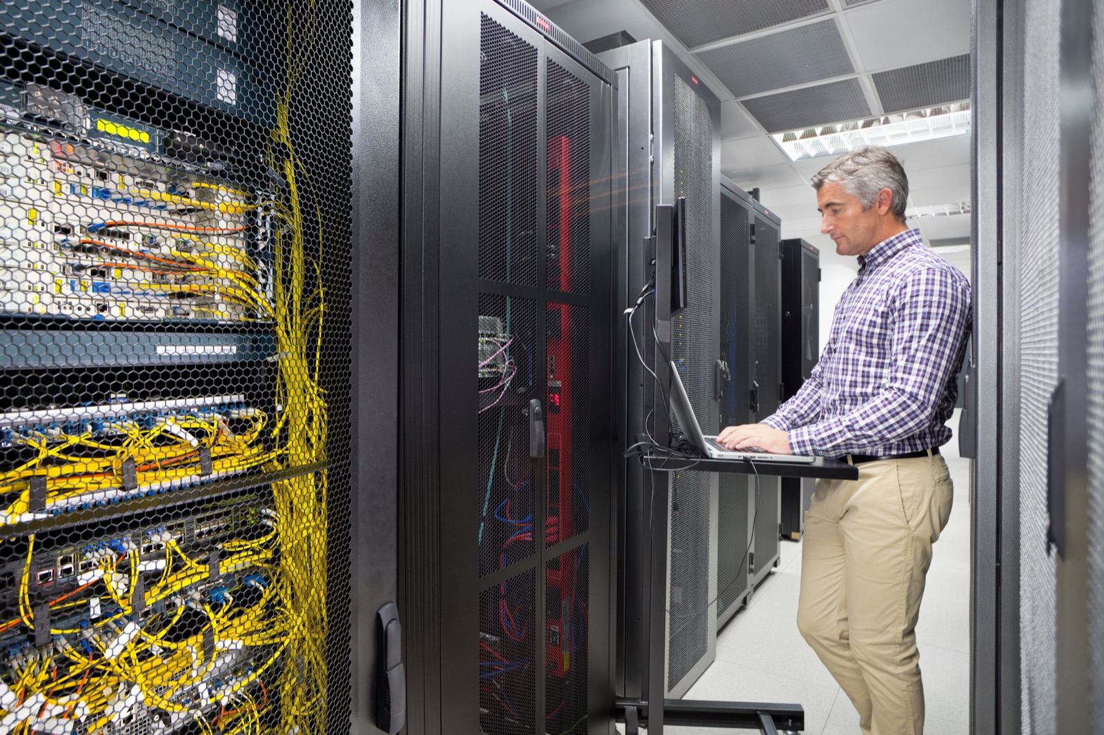 An engineer working on a laptop between server racks in a data centre
