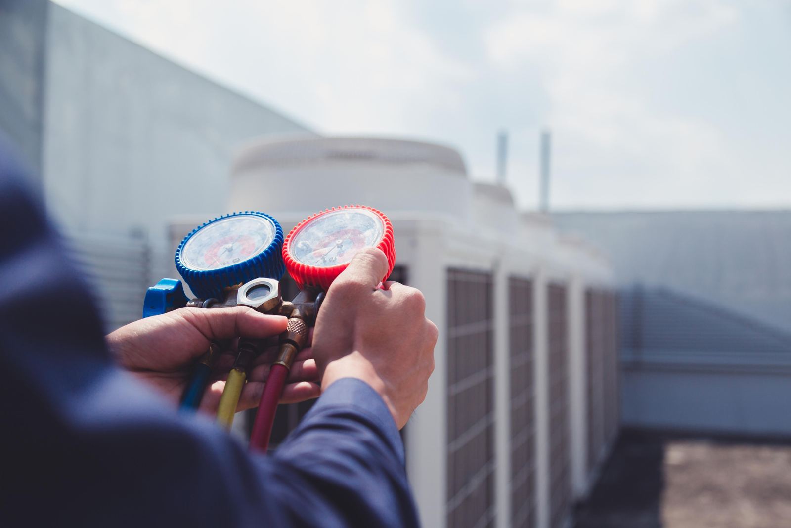 An HVAC technician reading the manifold gauges on a commercial rooftop air-conditioning unit