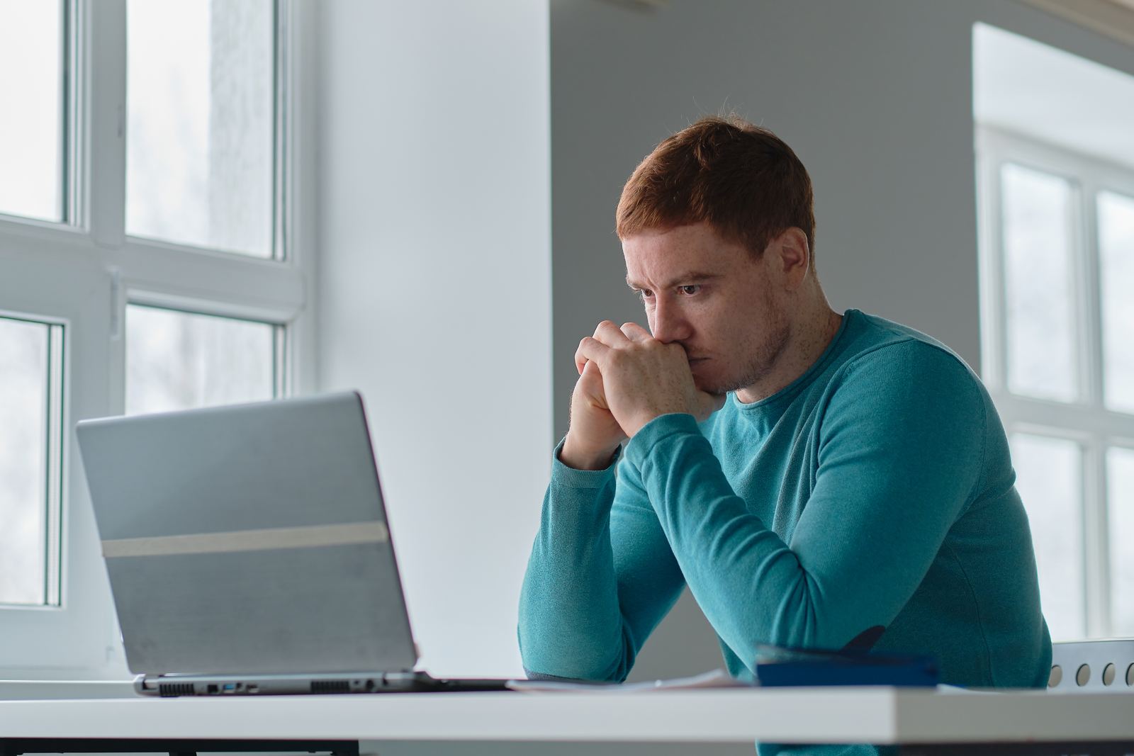 A man sitting in front of a laptop with his hands at his face, looking worried