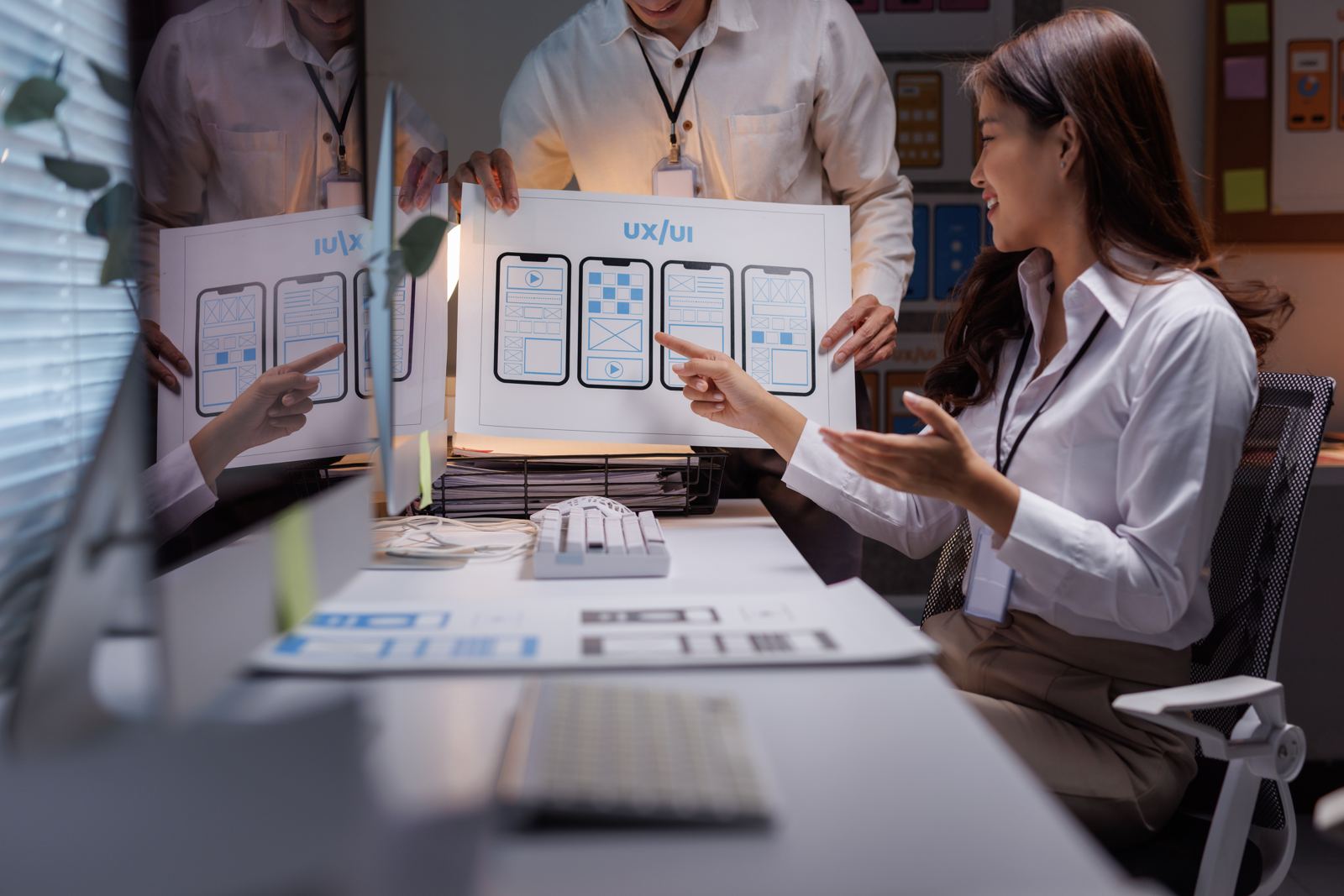 A woman pointing at printed screen designs while discussing them with colleagues at a desk