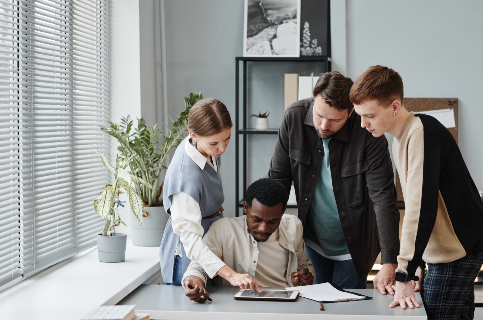 Four colleagues gathered around a desk, reviewing results on a tablet together