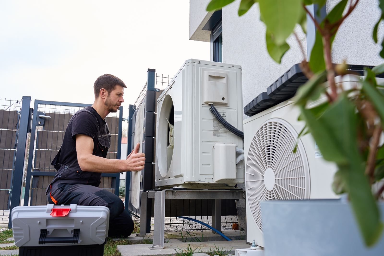 A technician installing an outdoor heat pump unit next to a house