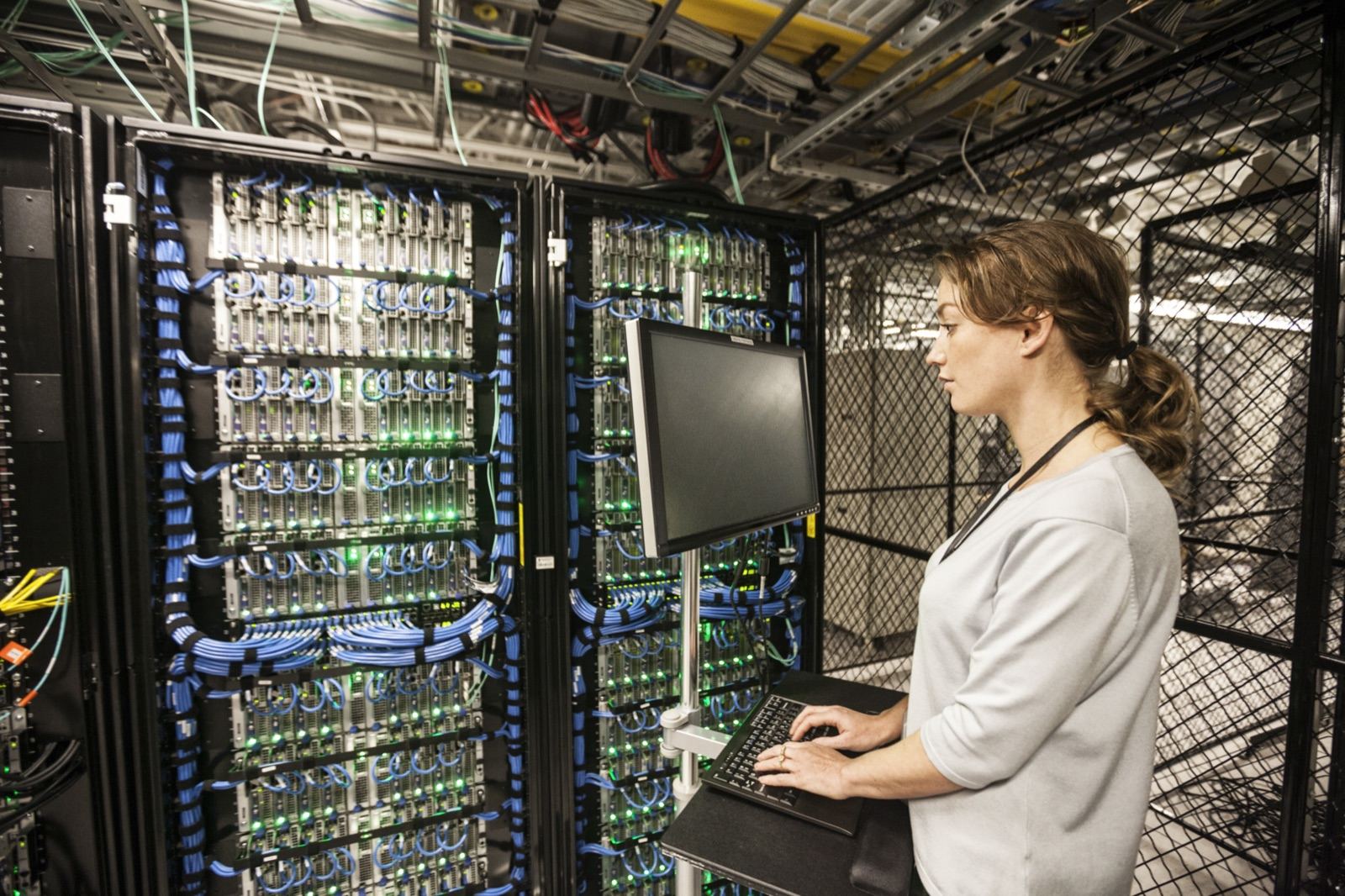 A woman working at a terminal between server racks full of network cables