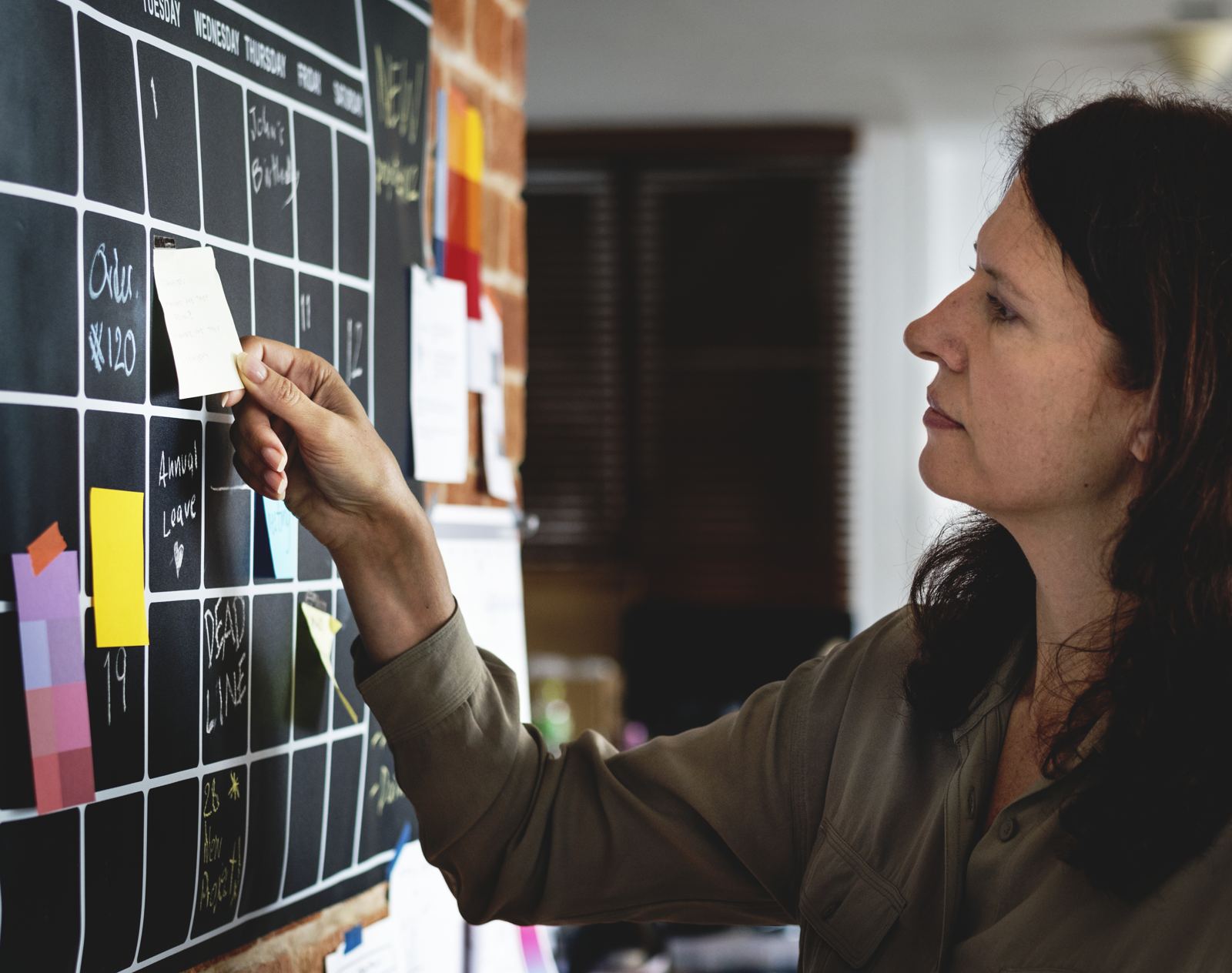 A woman pinning a note to a large wall calendar while planning
