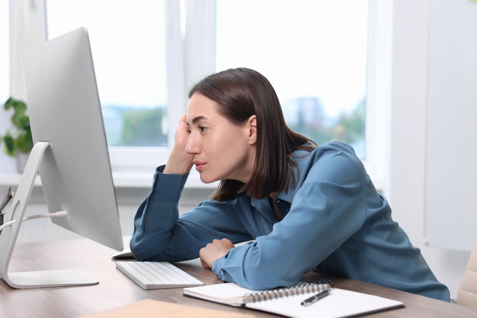 A woman resting her head on her hand, staring at a computer screen and waiting